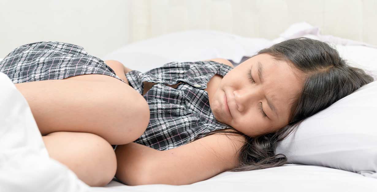 A child laying in bed holding their stomach.